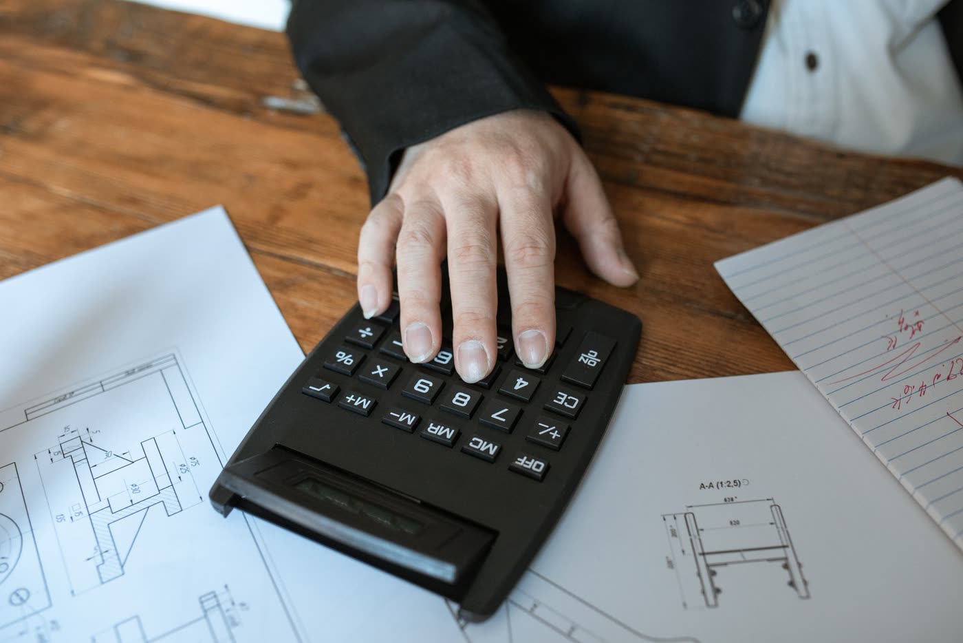 A hand working out figures on a calculator over building plans