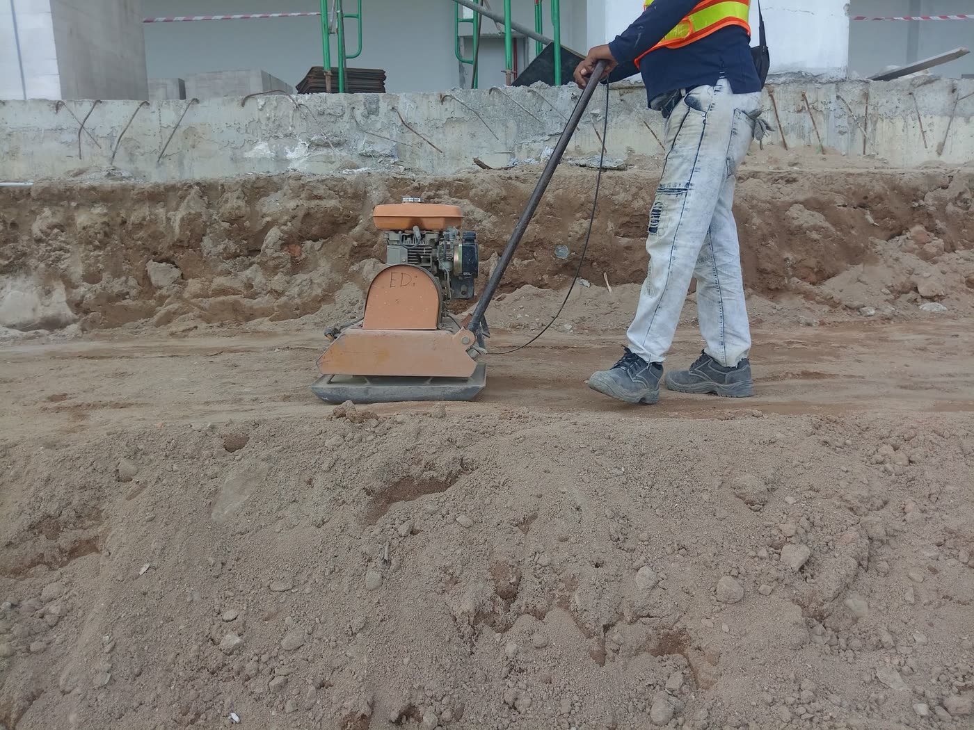 A construction worker running a plate compactor over prepared ground