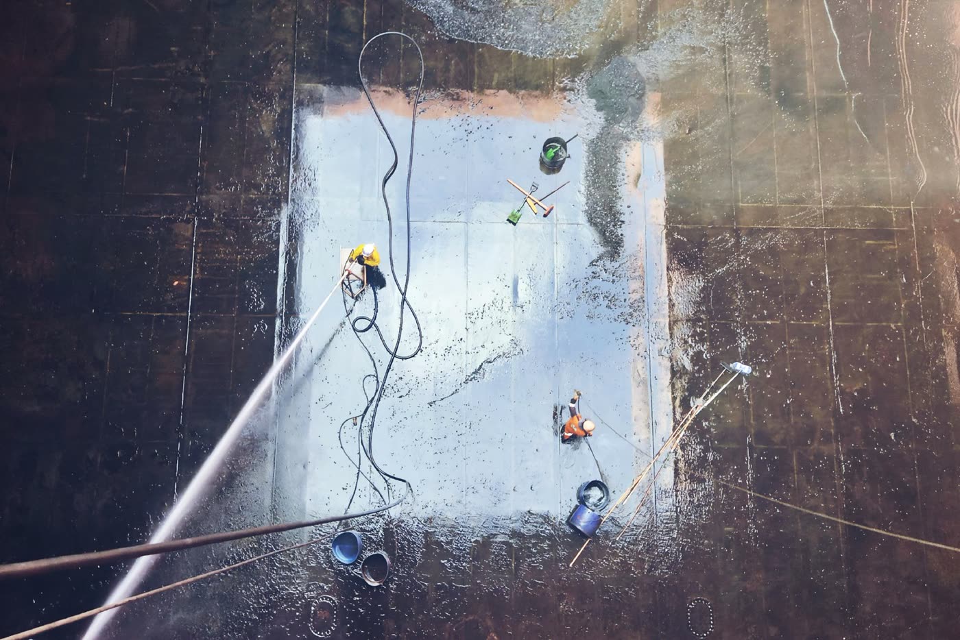 Overhead view of workers cleaning a large paved surface with water hoses