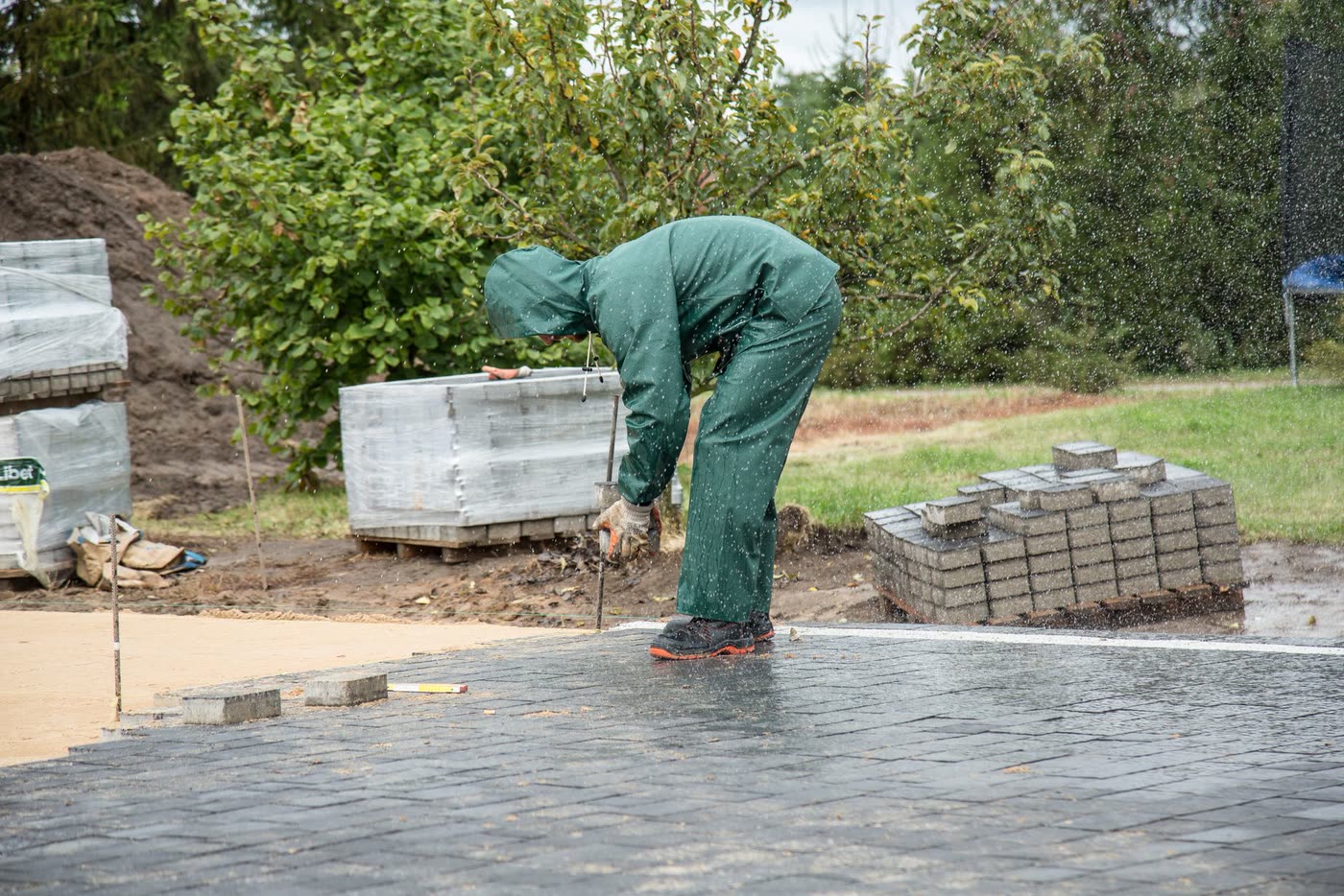 A worker in protective gear laying paving stones on a wet day