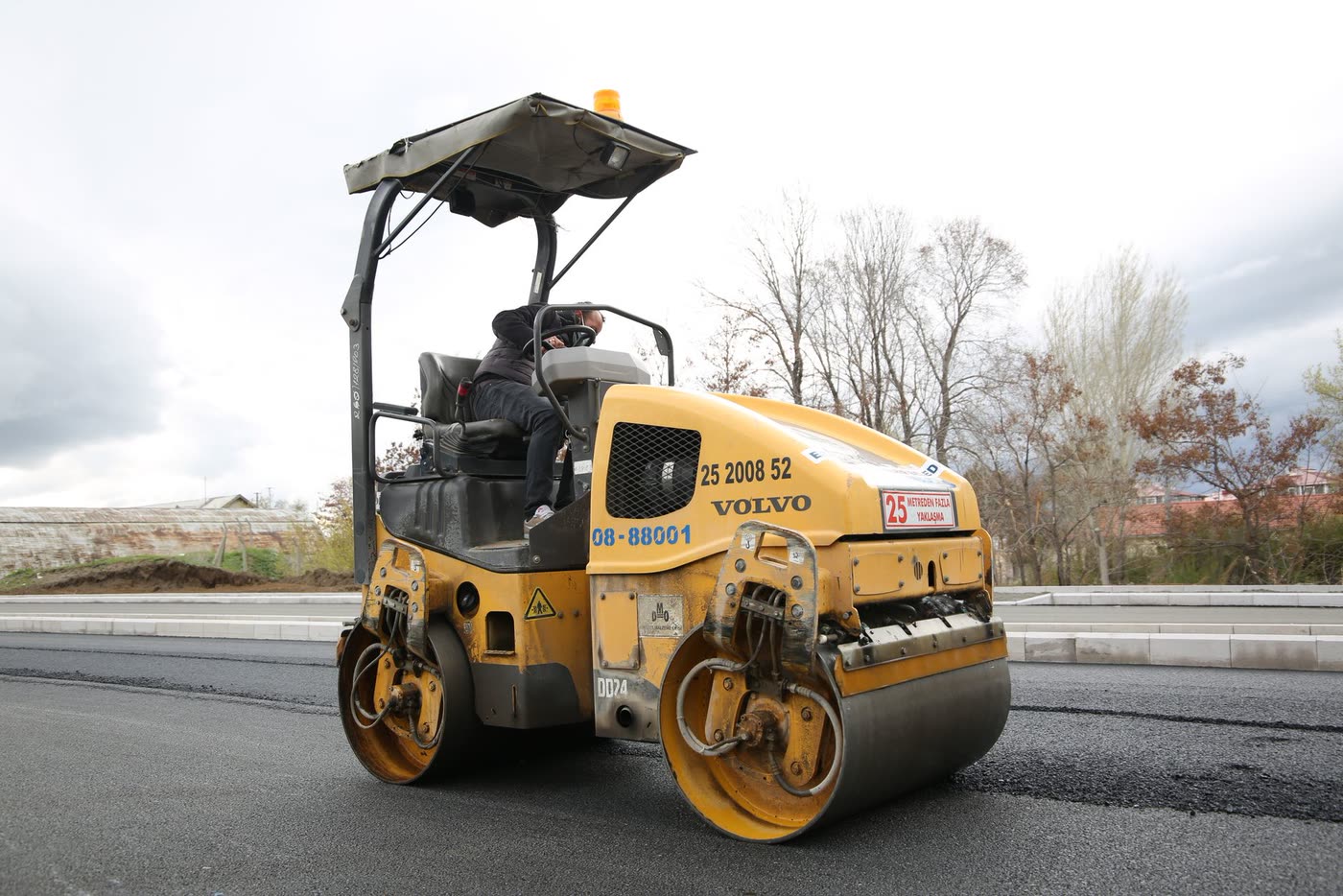 A road roller compacting fresh asphalt, with the operator at the controls