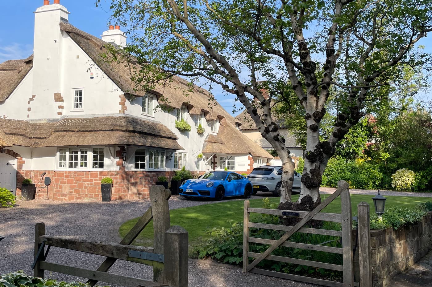 A thatched English cottage with a gravel driveway, five-bar gate and stone boundary wall