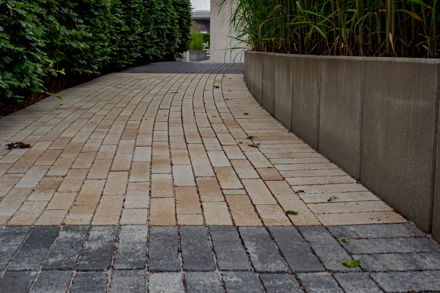 Permeable block paving with open, grit-filled joints, curving between a hedge and a concrete planter
